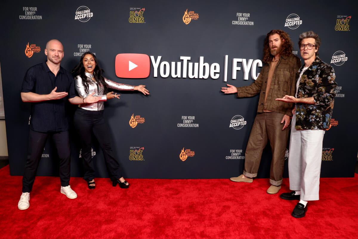 A photo of four people standing on a red carpet with "YouTube FYC" on the backdrop