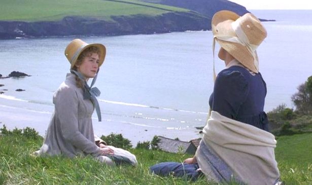Two women sit on grass overlooking the sea