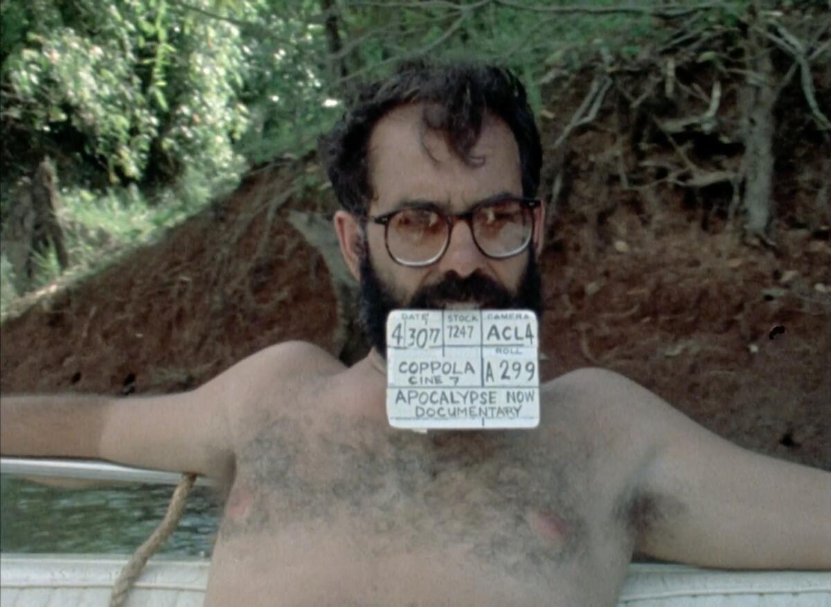 A shirtless man sits with a card in his teeth.