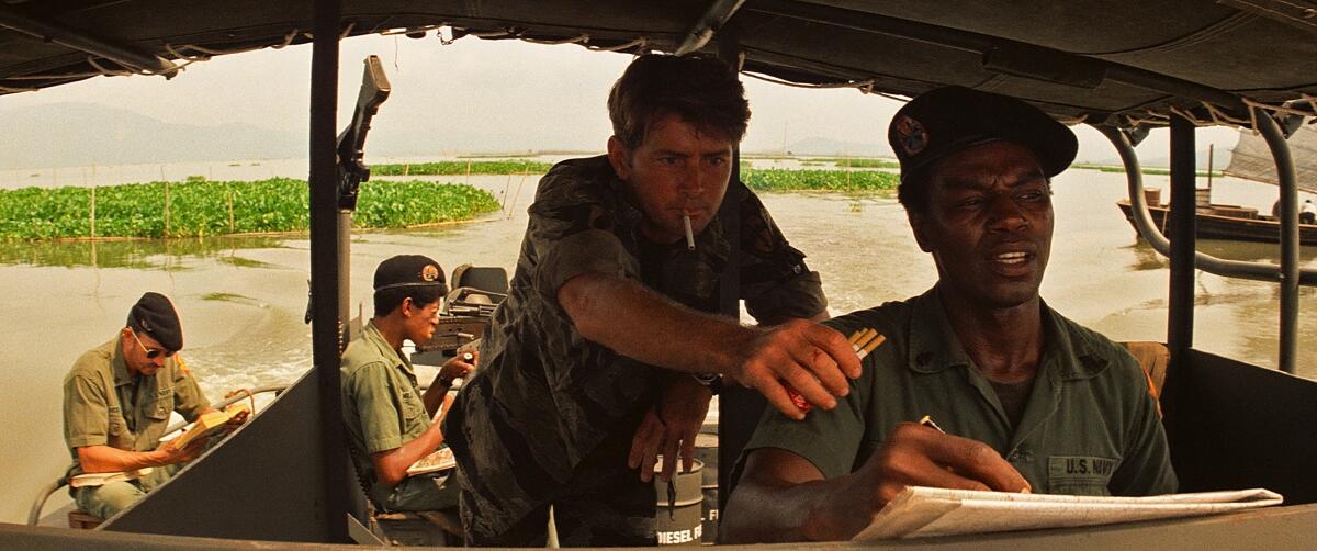 Four men ride on a PT boat upriver in Vietnam.