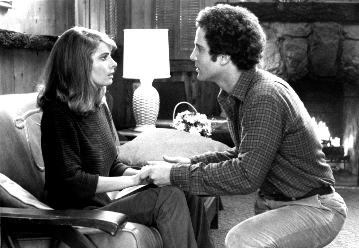 A couple holds hands in discussion in their living room.