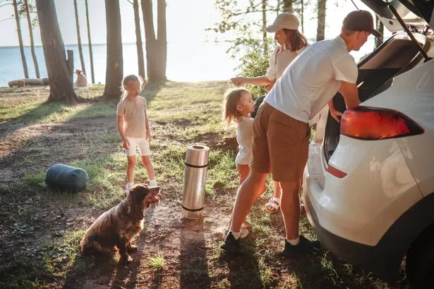 Traditional Family with Two Children and Dog Unpacking Car Trunk at Camping Site with Tent. Nature Getaway with Kids