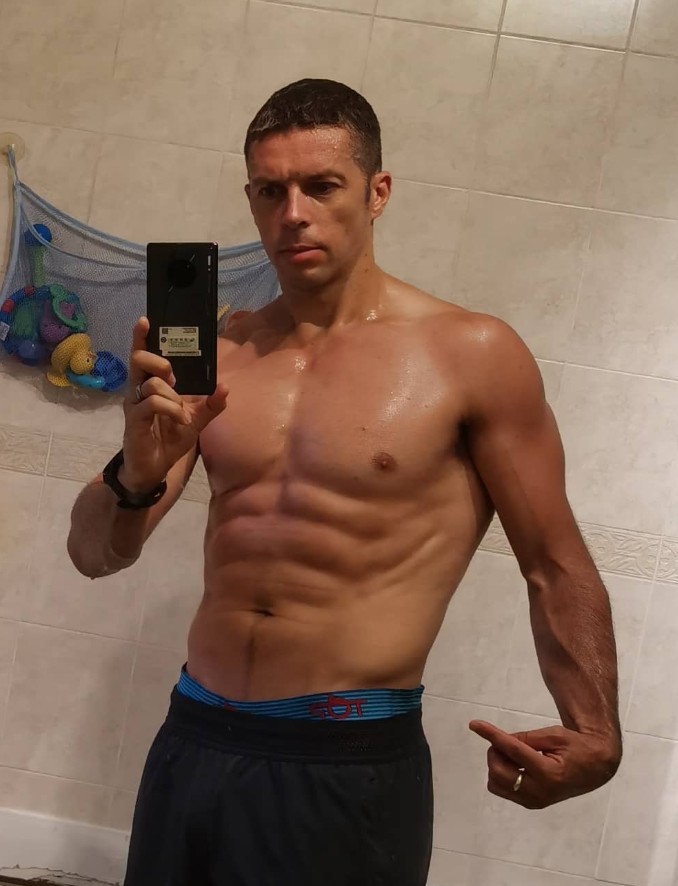 Self-portrait of a shirtless man taking a selfie in a bathroom.