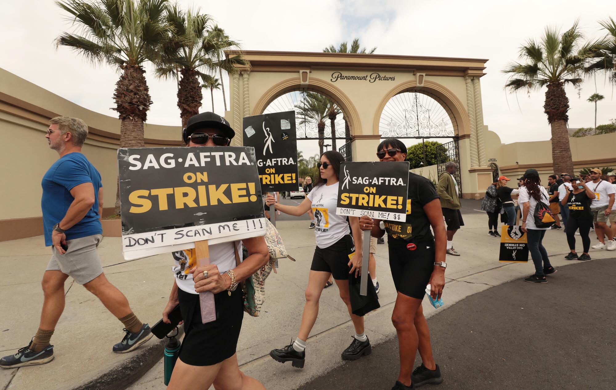 Actors march in protest outside a studio gate.