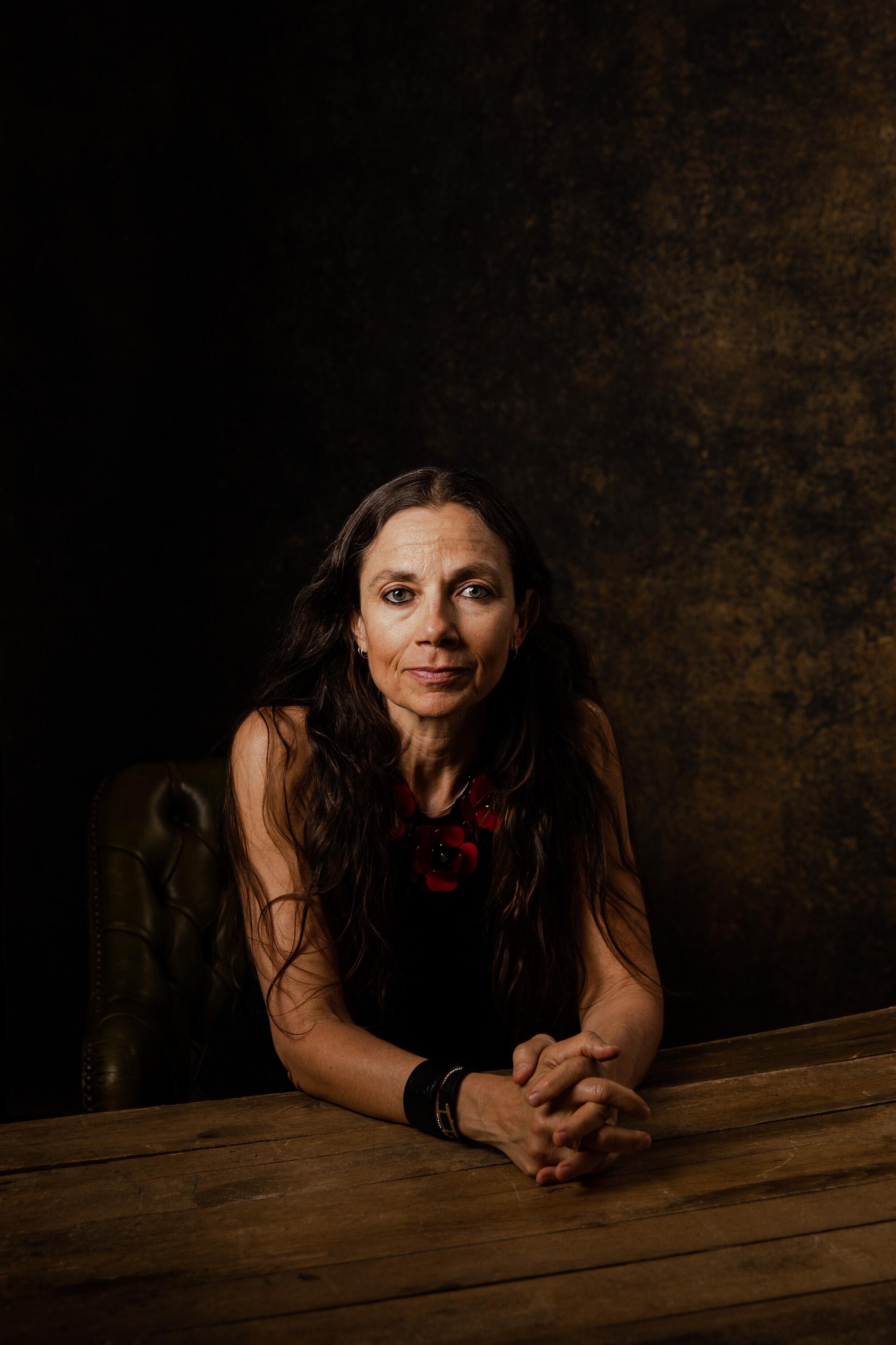 A woman in a dark top gazes into the lens.