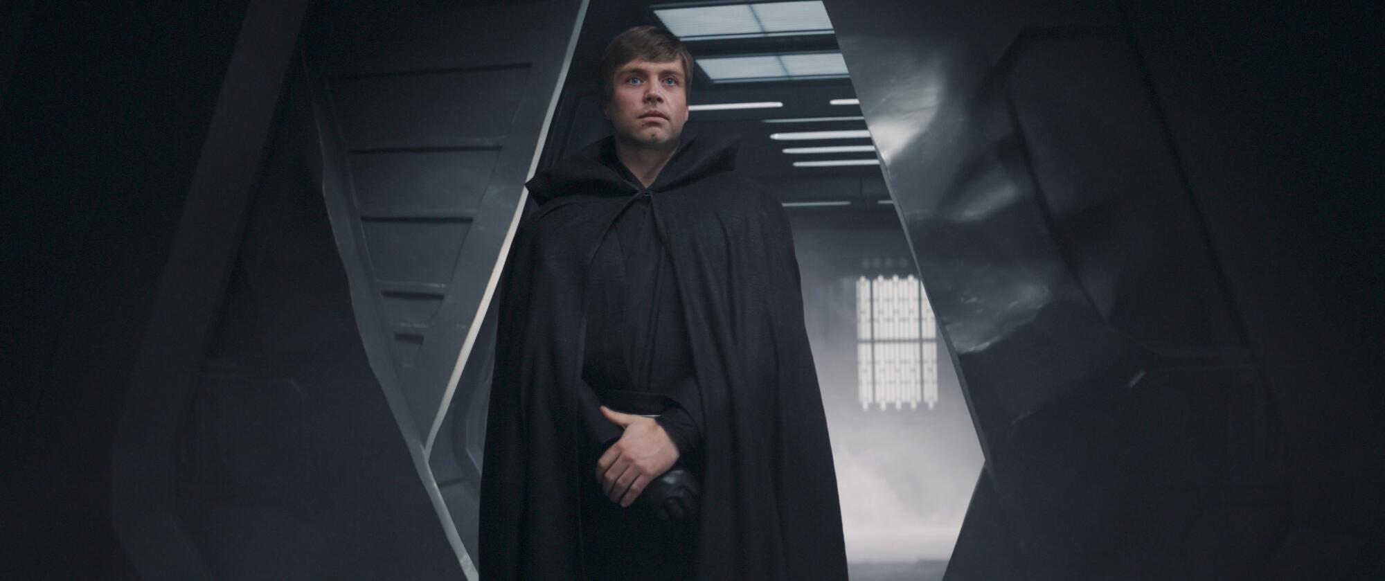 A young Jedi in black robes stands at a doorway.