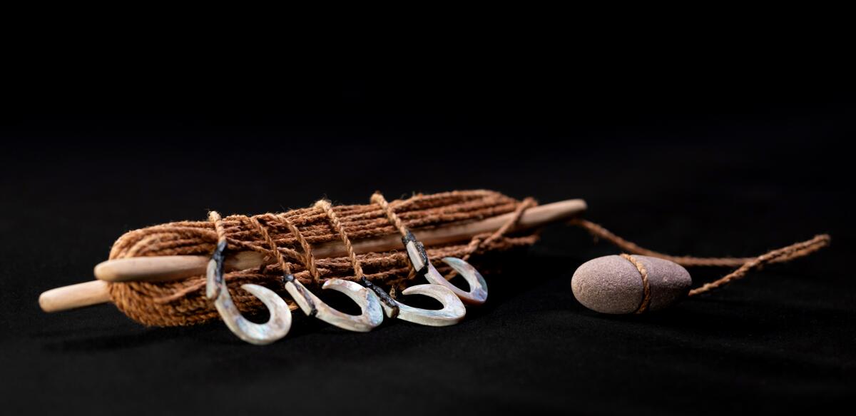 A coiled line with large silver hooks, attached to a smooth, palm-sized rock once used for fishing. 