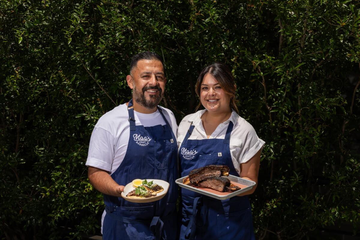 Andrew and Michelle Muñoz with beef ribs, beef rib tacos, and salsa outside in front of greenery.