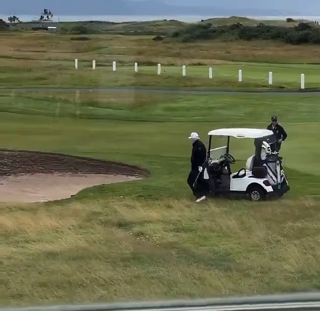 Golf caddy dropping a golf ball near a sand trap.