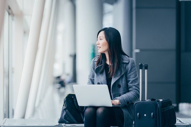 Young woman with suitcase looking away while working on her laptop at the airport.