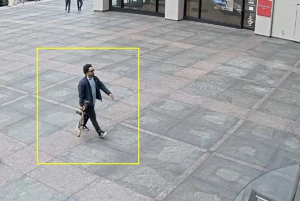 Security camera image of a man carrying a rifle walking outside a building.