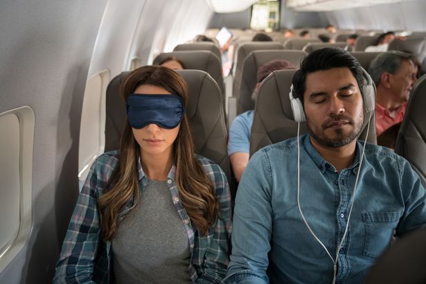 Image of woman wearing eyemask next to man wearing headphones on a plane