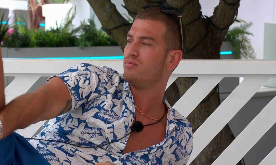 Man in a floral shirt sits outdoors and looks pensive.