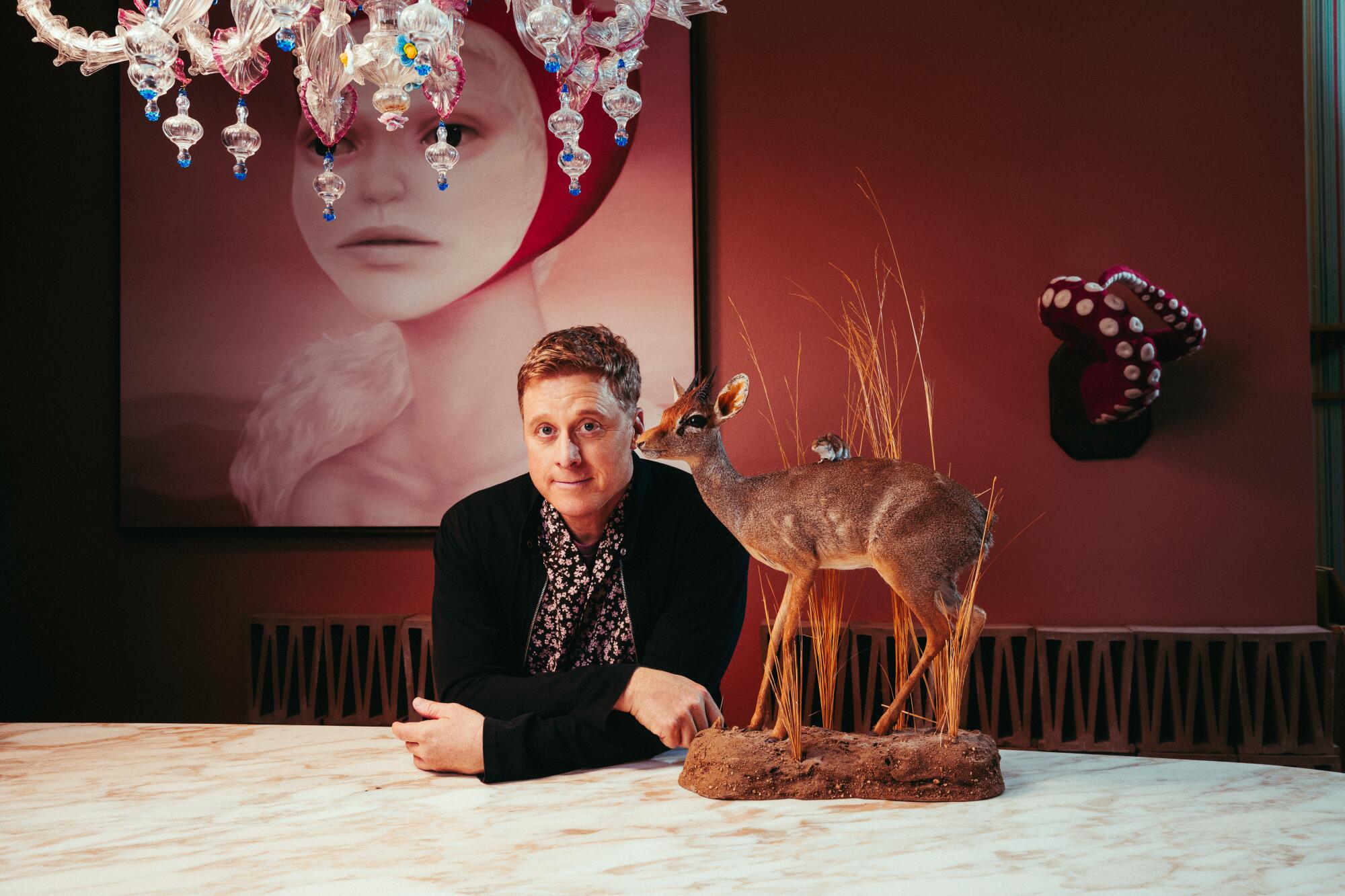 A man at a table with a taxidermized fawn set next to him.