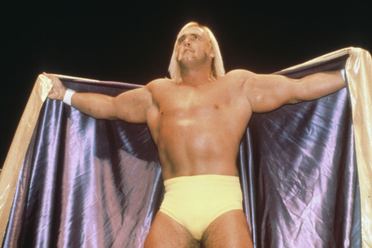 A man spreading a cape with his arms in yellow wrestling briefs.