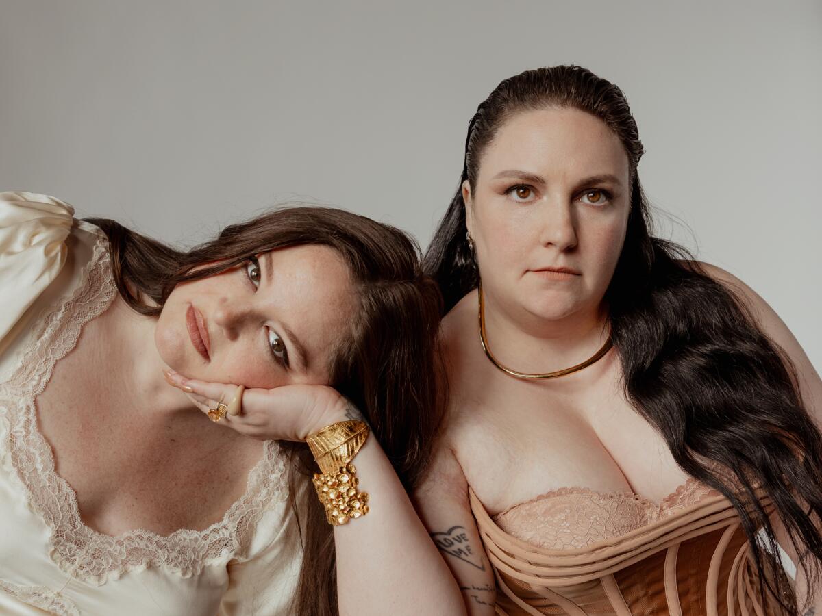 A woman, posing for a photo, rests her head in the palm of another woman's hand