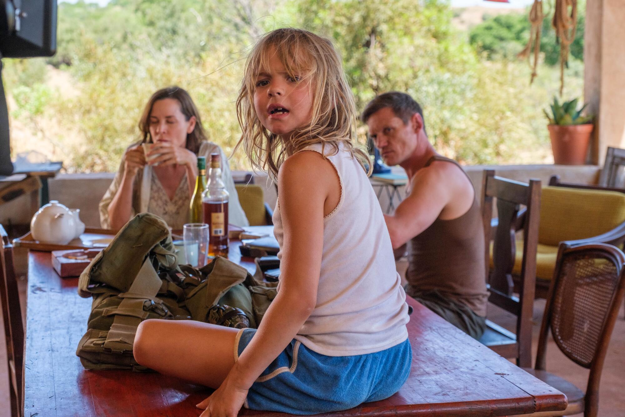A family sits at a dining table. their daughter sitting on the table.
