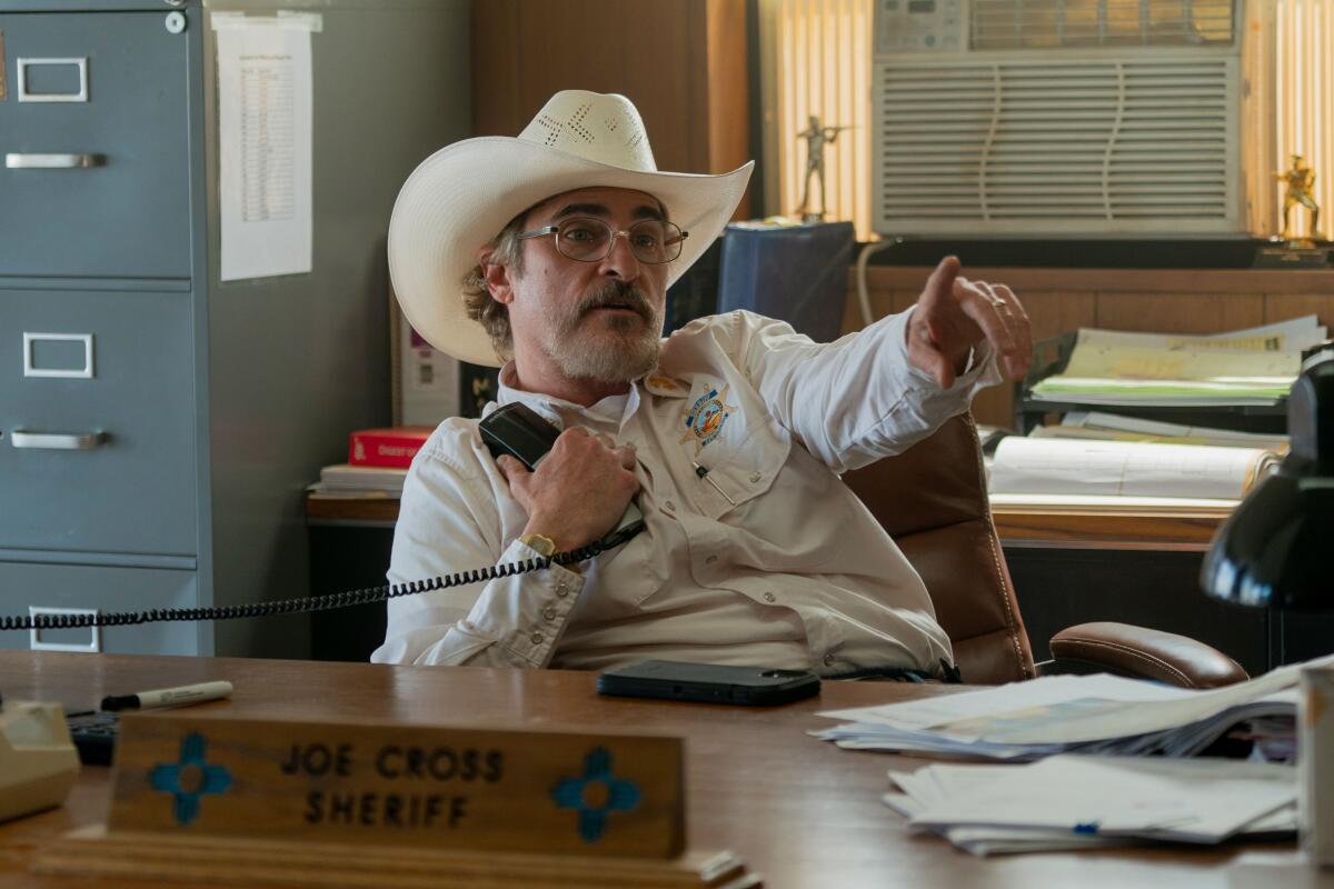 A sheriff in a white hat sits at his desk on the phone.