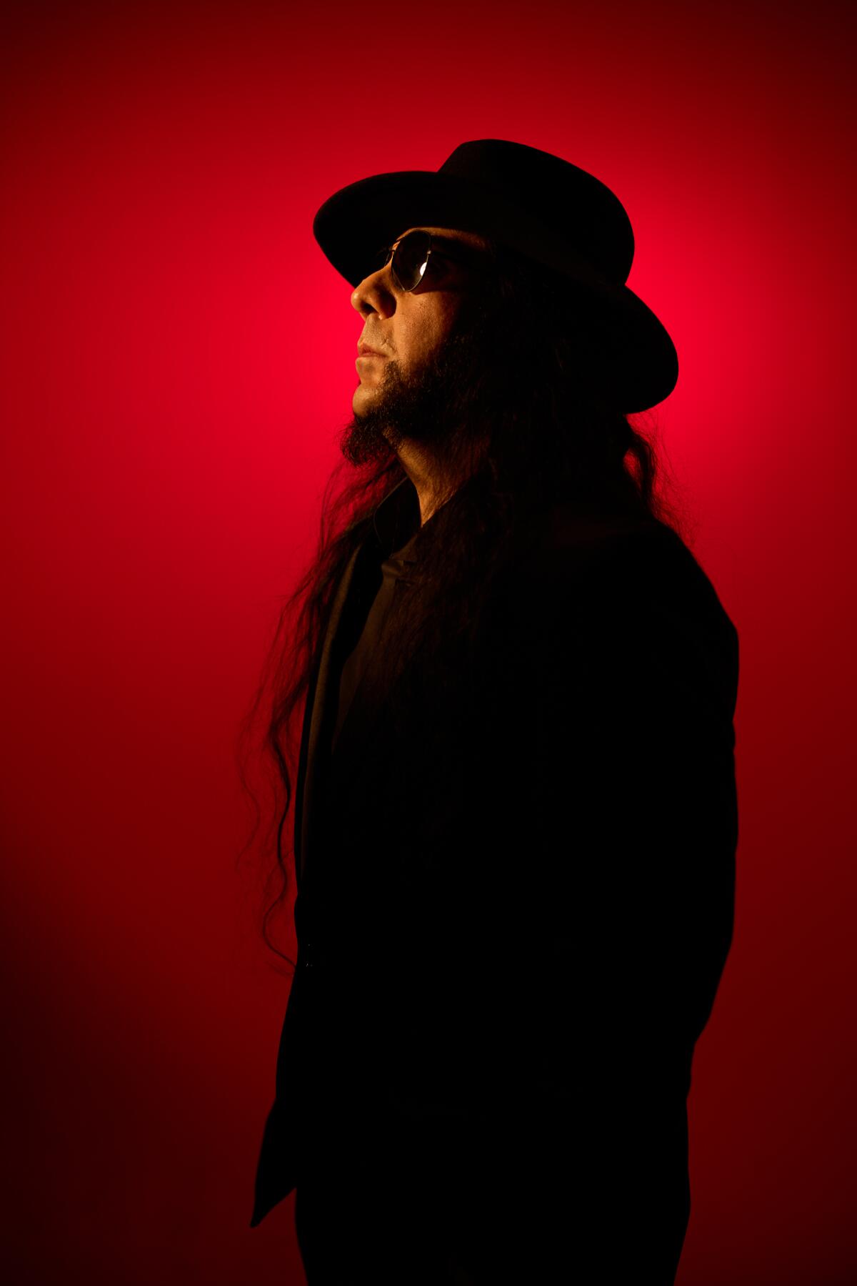 Man standing sideways in a dark suit behind red background