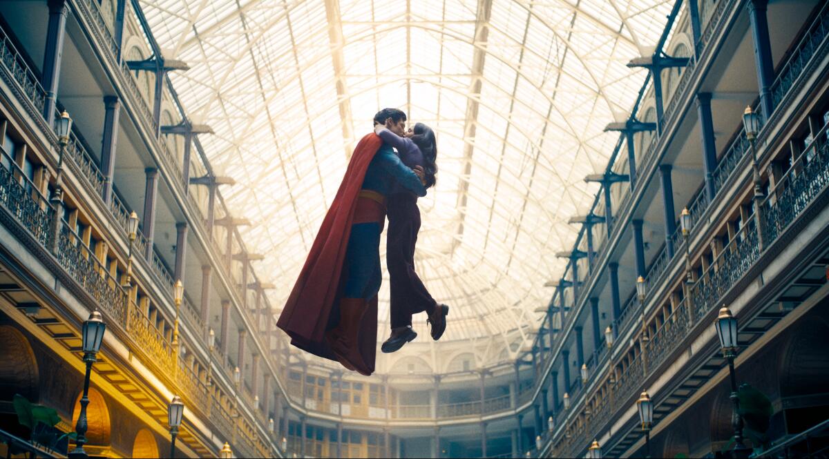 Superman and Lois Lane float in midair with their arms around each other inside a building with a curved glass-pane roof