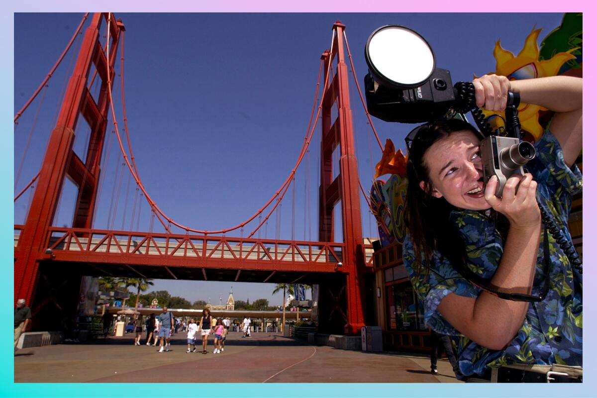 Park photographer photographs visitors entering Disney's California Adventure with Golden Gate Bridge entrance behind her.