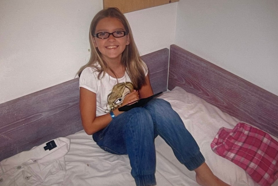 Photo of a young girl sitting on a bed, holding a tablet.
