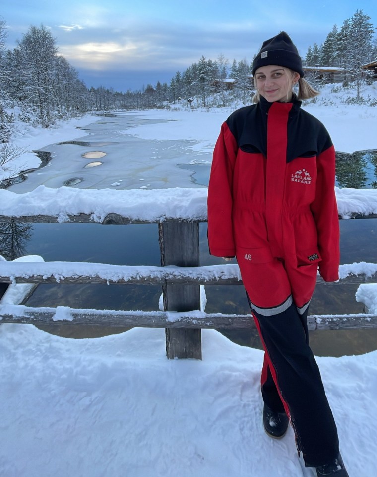Woman in red snowsuit standing by a snowy river.