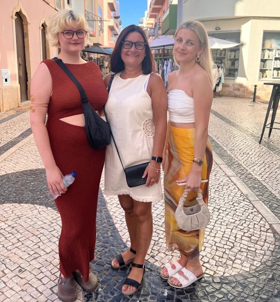 Three women standing on a cobblestone street.