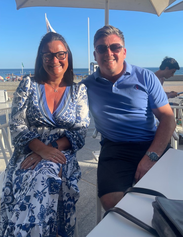 Couple sitting at an outdoor table by the ocean.