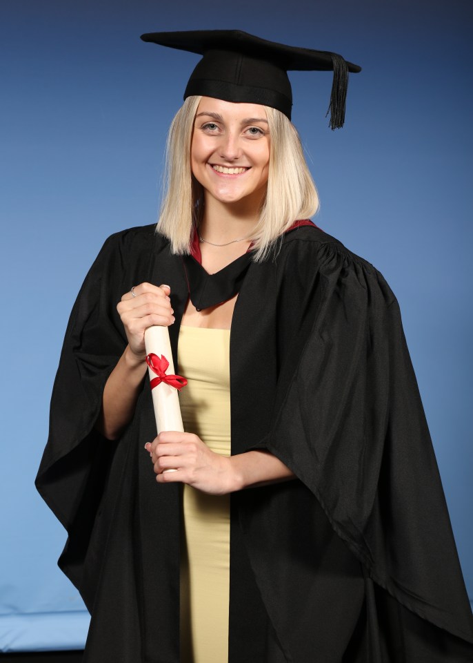 A smiling blonde woman in graduation attire holds her diploma.