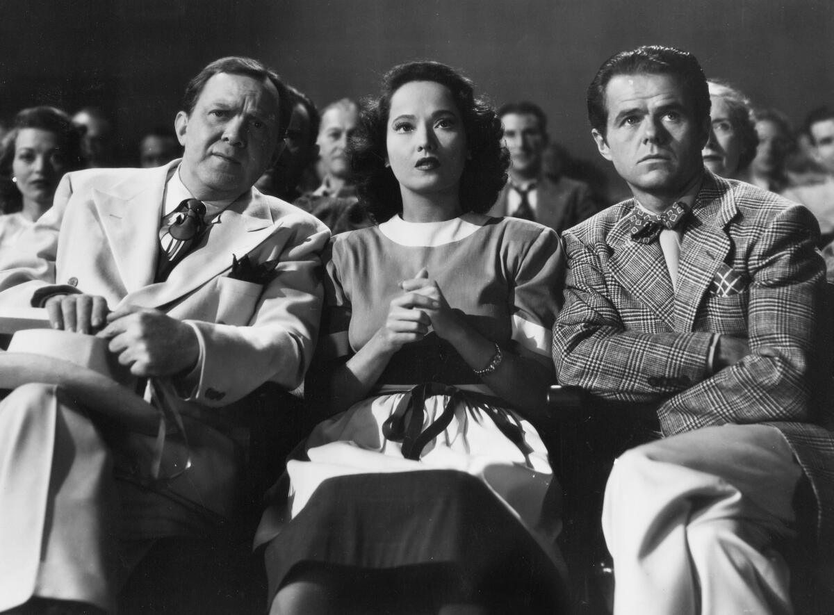 A woman sits between men in suits.