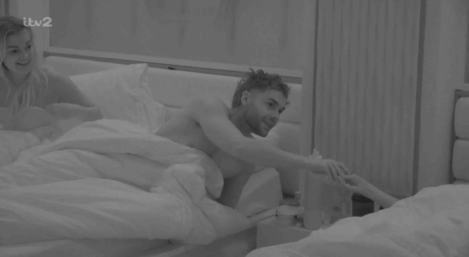 Screenshot of a couple in bed, one reaching for a condom.