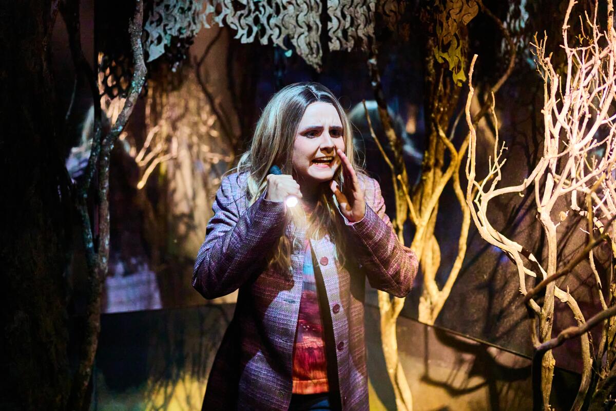 An actor with a flashlight in a scene designed to look like the woods.