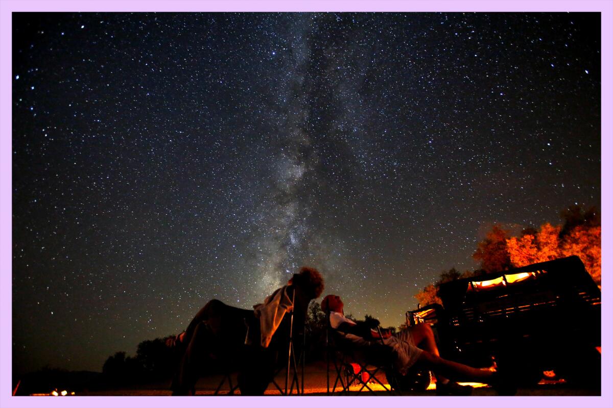 Two people sitting in camp chairs look up at a brilliant night sky twinkling with stars.