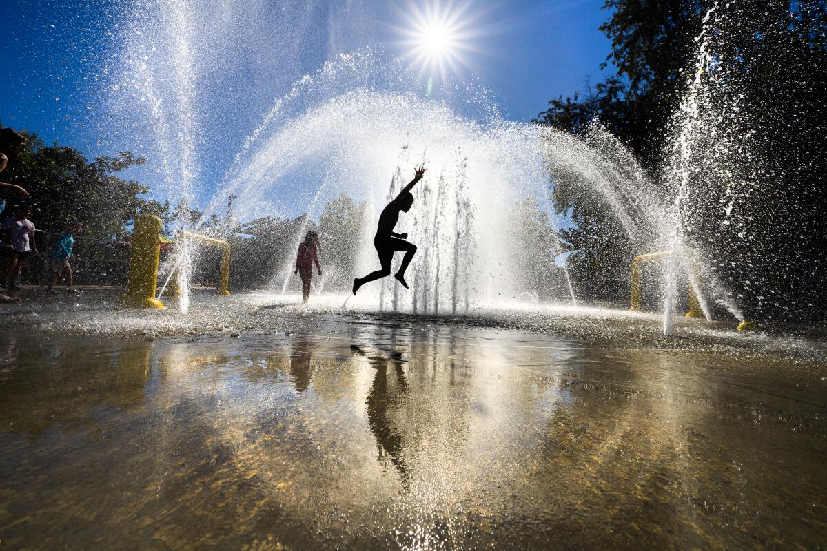 The afternoon sun silhouettes a child as he jumps through a fountain. 