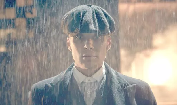 A man in a flat cap walks through the rain