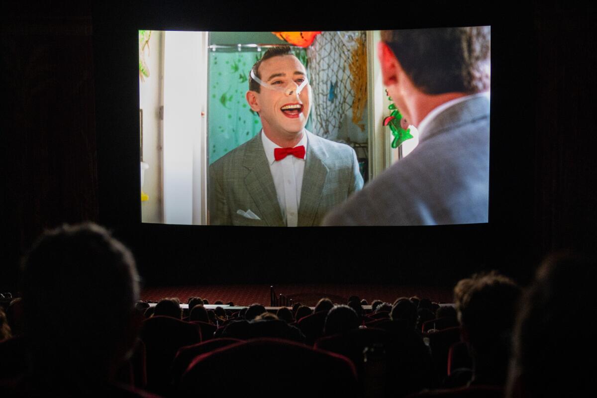 A man in a gray suit and red tie entertains viewers watching in a cinema.