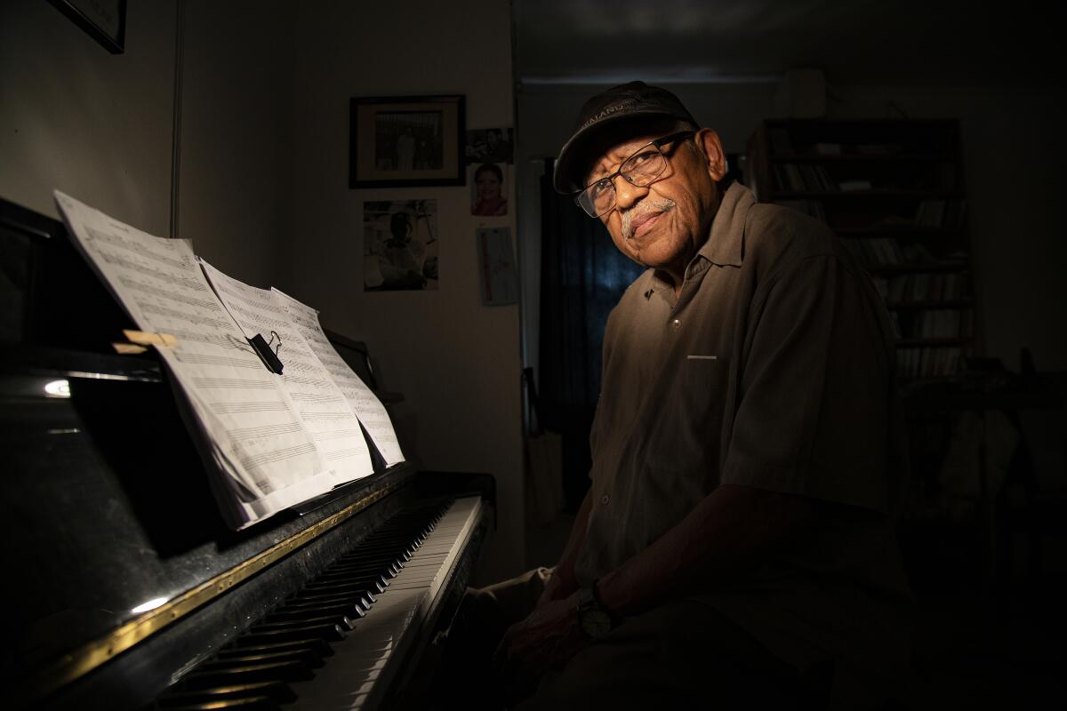 An elderly man in glasses poses with sheet music.