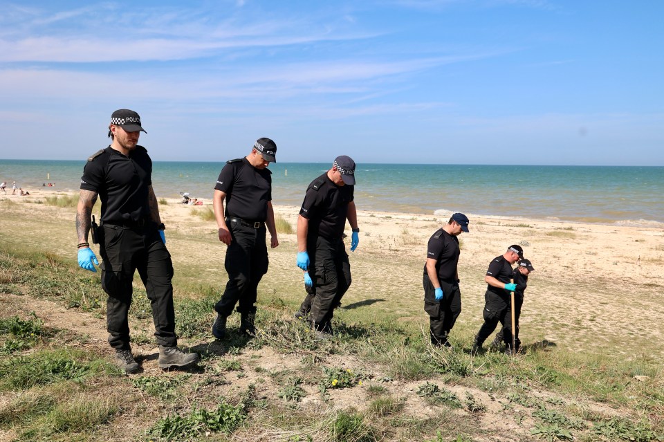 Police officers searching a beach.