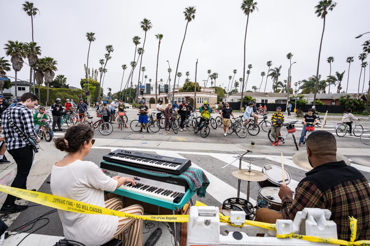 Musicians play music as cyclists and pedestrians ride and walk on the street.