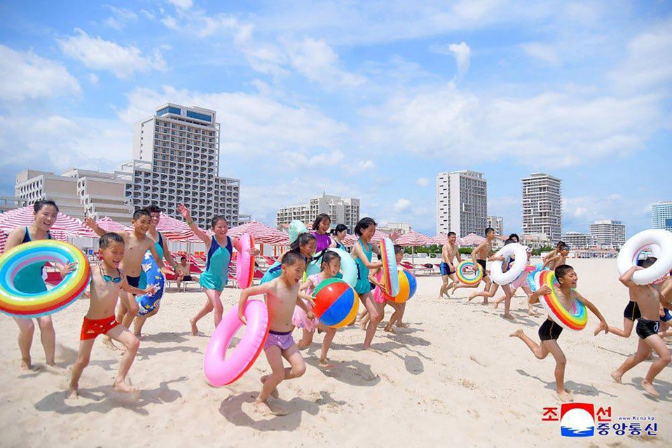 Children playing on a beach with inflatable rings and beach balls.