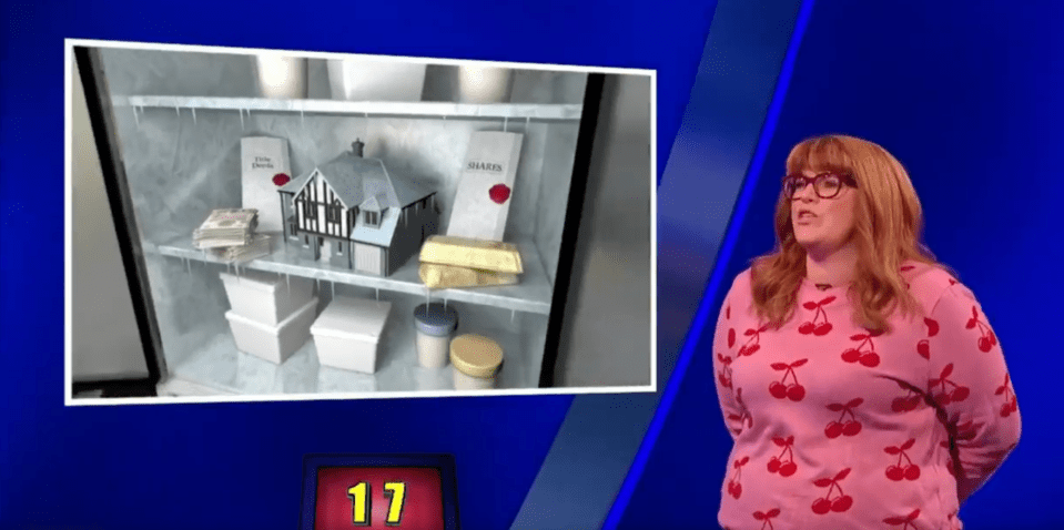 Screenshot of a game show contestant standing next to an image of a shelf containing a house model, gold bars, and documents.