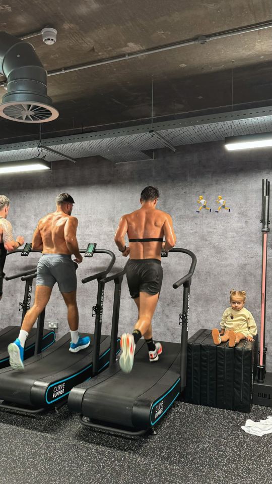 Three men running on treadmills in a gym, with a toddler sitting nearby.