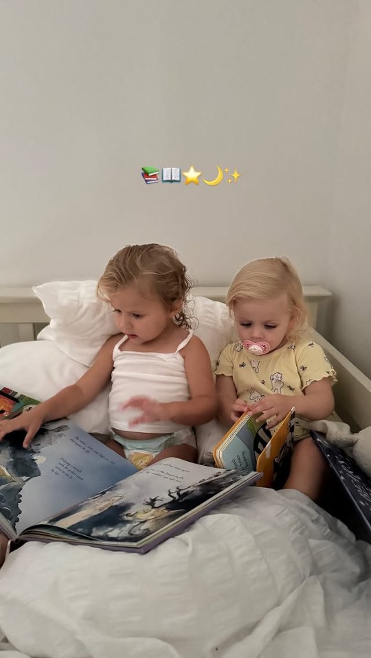 Two toddlers reading books in bed.