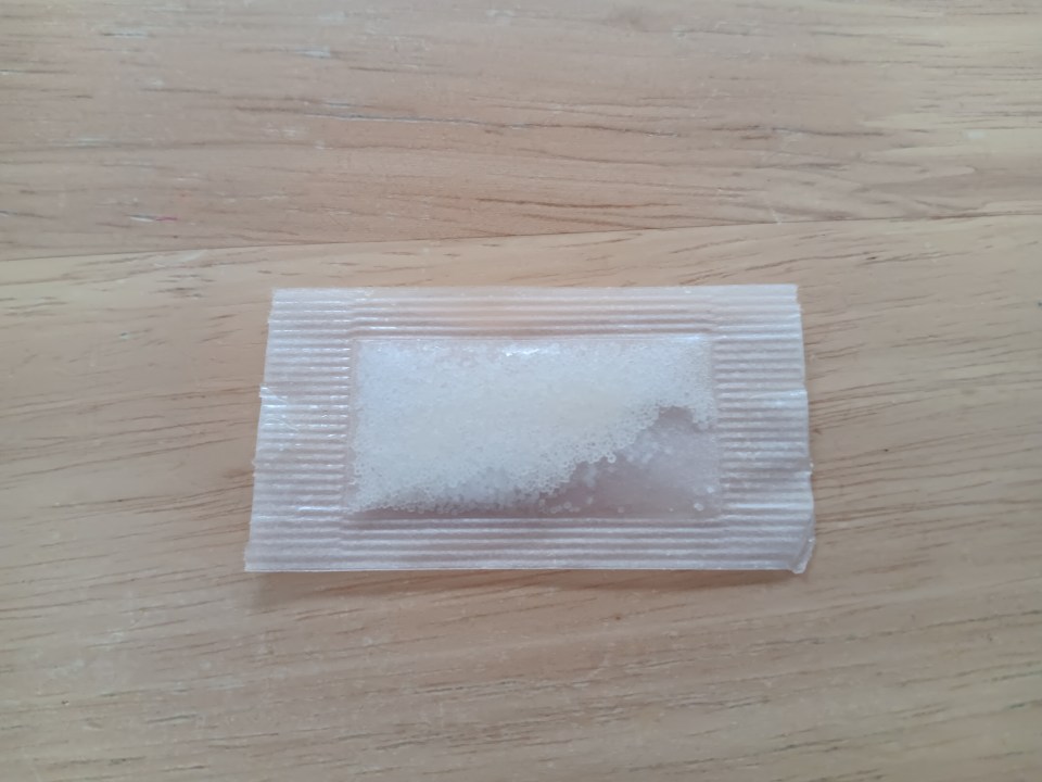 A packet of white crystals on a wooden surface.
