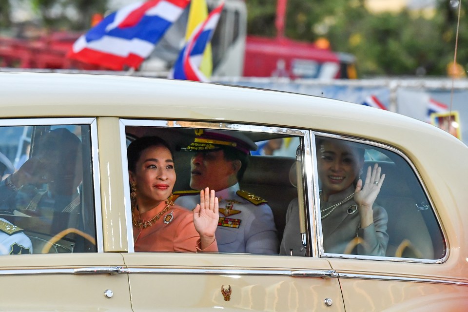 The Thai King, Queen, and Princess Bajrakitiyabha Mahidol waving from a car.