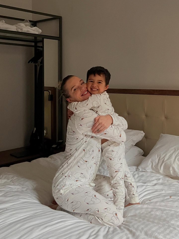 Woman and child in matching swan pajamas hugging on a bed.
