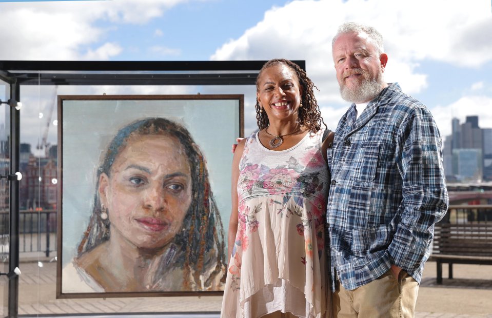 Photo of a couple standing in front of a portrait of a woman.