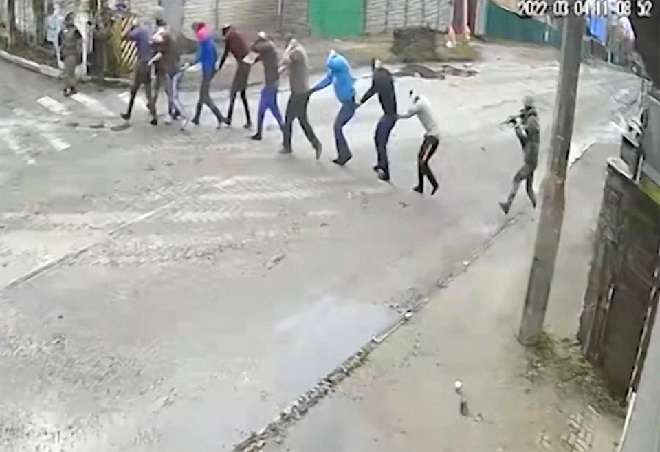 Civilians being marched down a street by a soldier carrying a rifle.