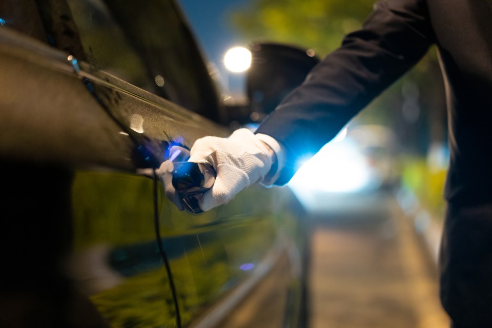A gloved hand opens a car door at night.